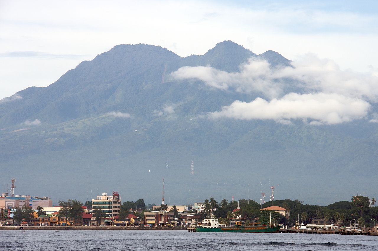 Shot of a city by the sea, with a towering mountain in the background