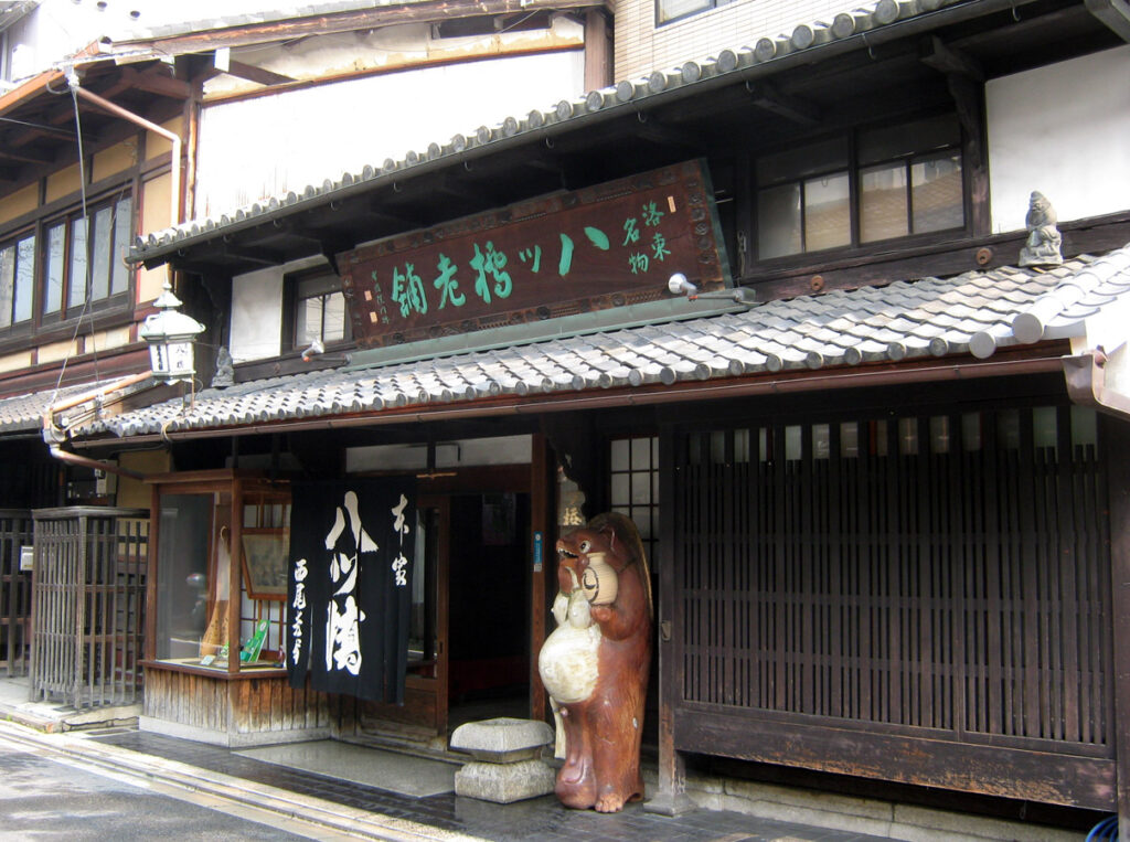 A tanuki statue outside the Honke Nishio Yatsuhashi sweet shop in Kyoto. By ja:利用者:Mariemon - ja:ファイル:Nishio5538.JPG, CC 表示 3.0, https://commons.wikimedia.org/w/index.php?curid=44994634